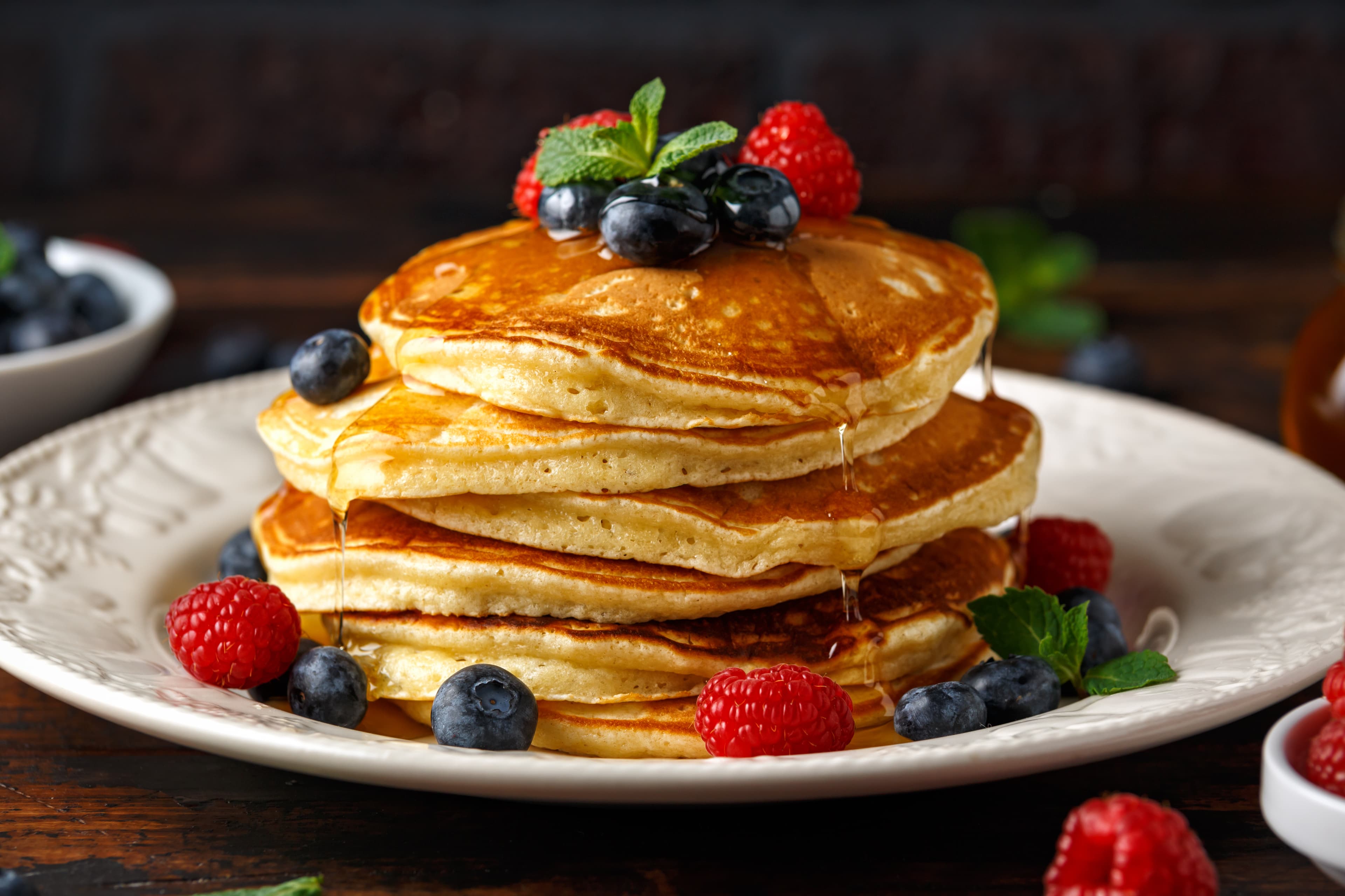 Golden pancakes topped with blueberries, raspberries, mint, and syrup